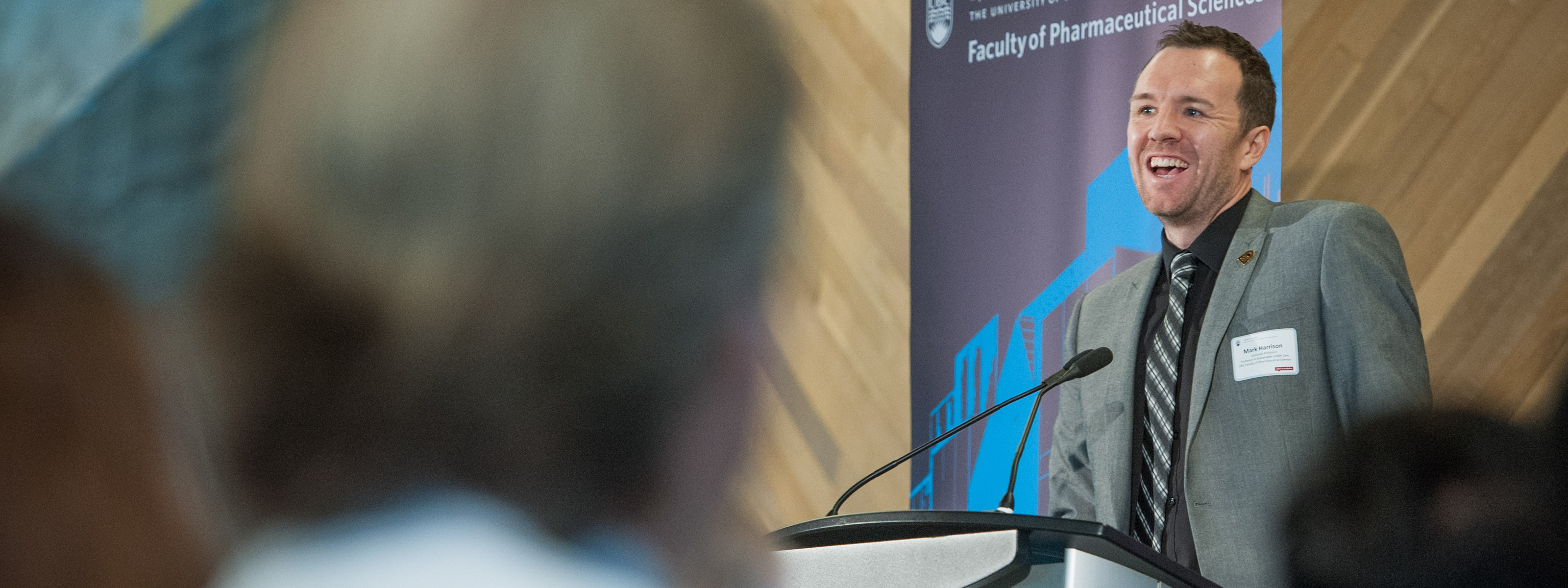 A health care professional speaking at a podium, with a Pharm Sci banner in the background.