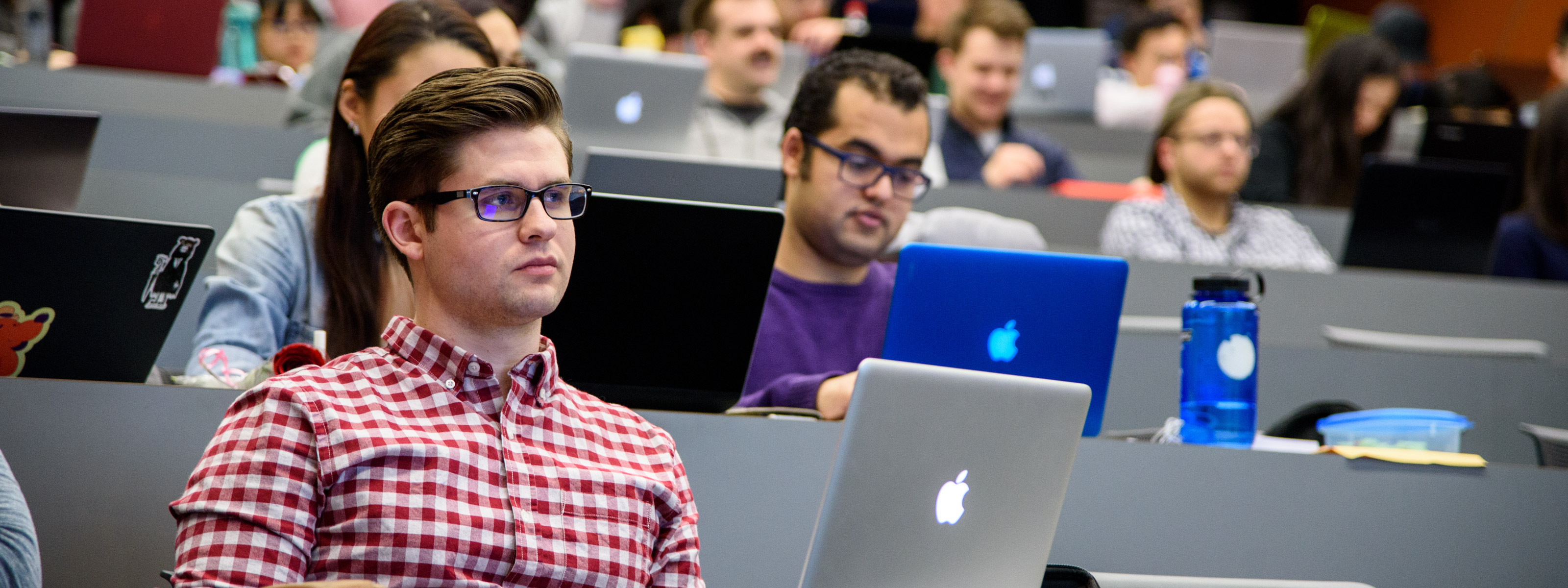 Students with laptops sitting in tiered rows in a lecture theatre.