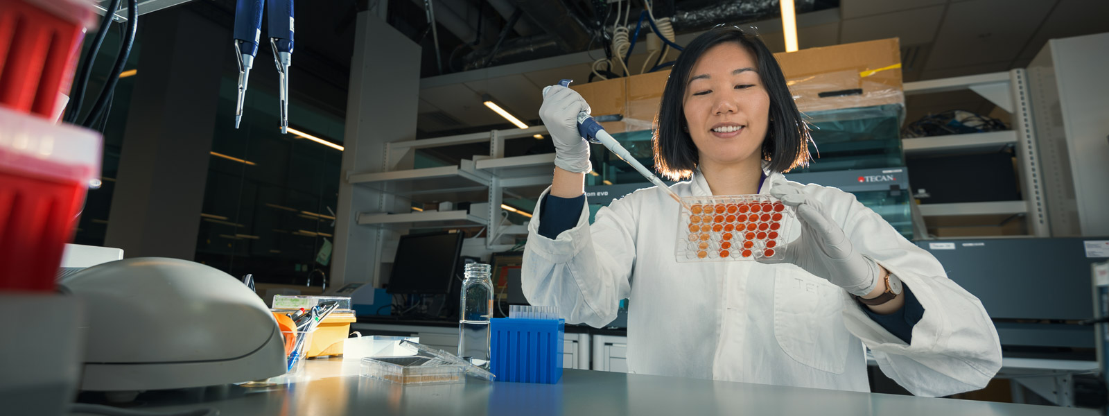 A researcher holding a tray with one hand and a syringe with the other.