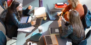 Three people sitting and working at a long table.
