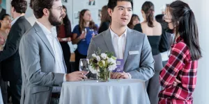 Three people standing at a table and mingling at an event.