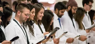 A group of pharmaceutical sciences students reading from pamphlets at their inaugural White Coat welcoming ceremony. 