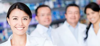 Four pharmacists looking at the camera; the woman in the foreground is smiling and the three in the back are out of focus.