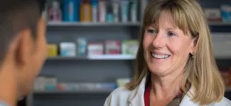 Two pharmacists speaking to each other, with a shelf of medications in the background.