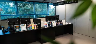 The empty front desk at the UBC Pharmacists Clinic; the desk contains computer screens and a number of brochures.