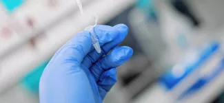 A close-up of a researcher, wearing blue gloves, holding a pipette.