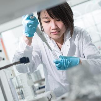 A researcher wearing a lab coat and focusing on conducting an experiment.