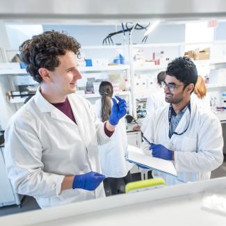Two students in lab coats, turning to speak to each other in a lab.