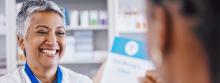 A pharmacist smiling and holding out a pamphlet to her patient.