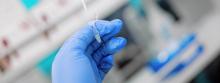 A close-up of a researcher, wearing blue gloves, holding a pipette.