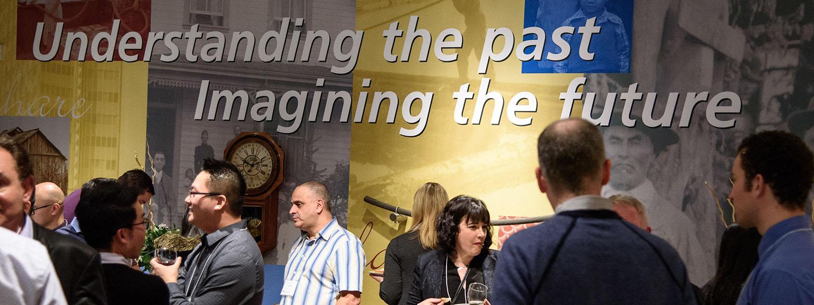 A collection of people mingling and conversing, overlaid with the text "Understanding the past, imagining the future".