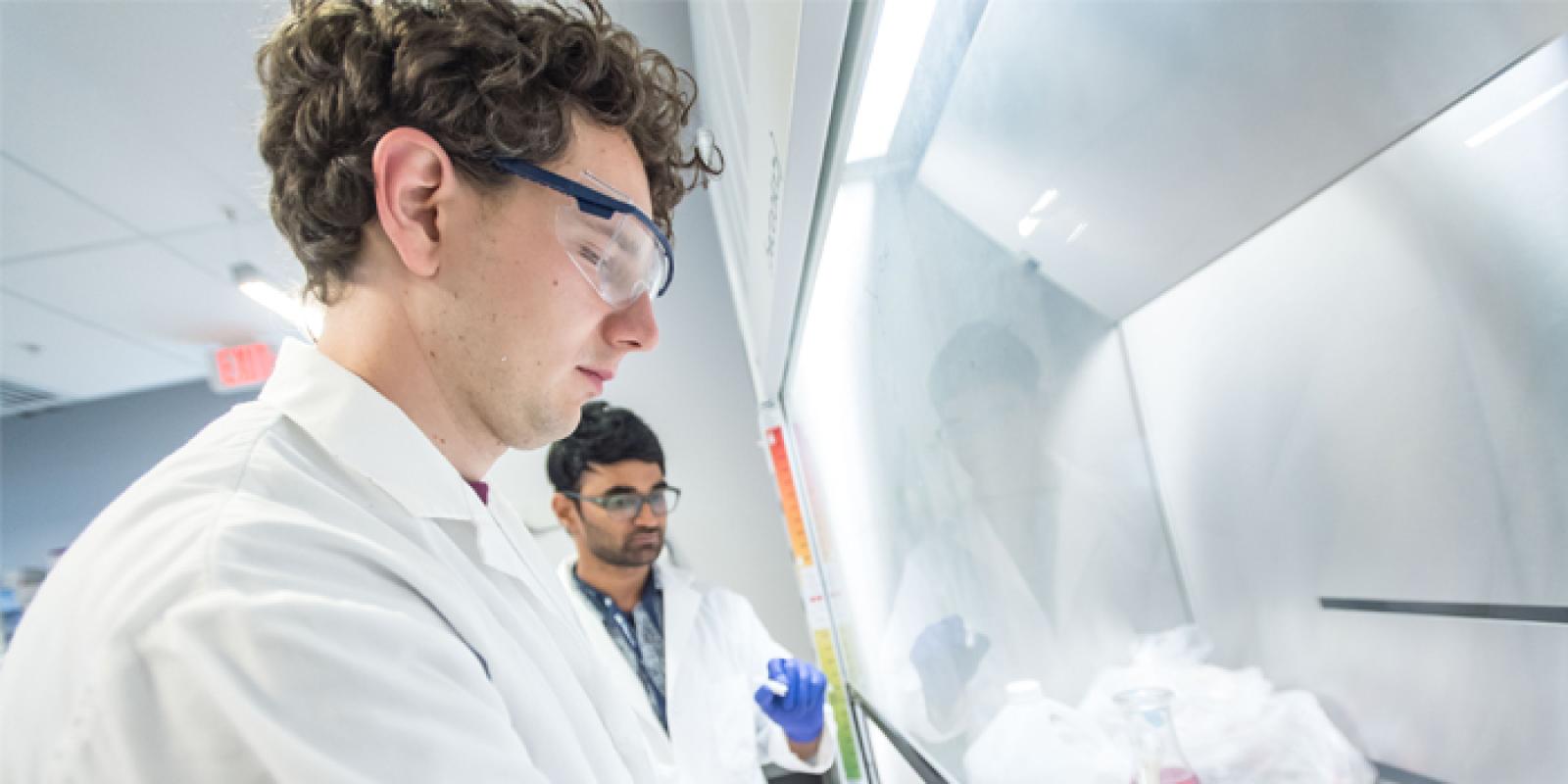 Two students wearing lab coats, conducting research in a lab.