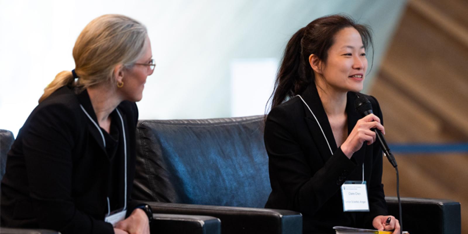 Two health care professionals conversing during a presentation; the woman on the right holds a microphone.