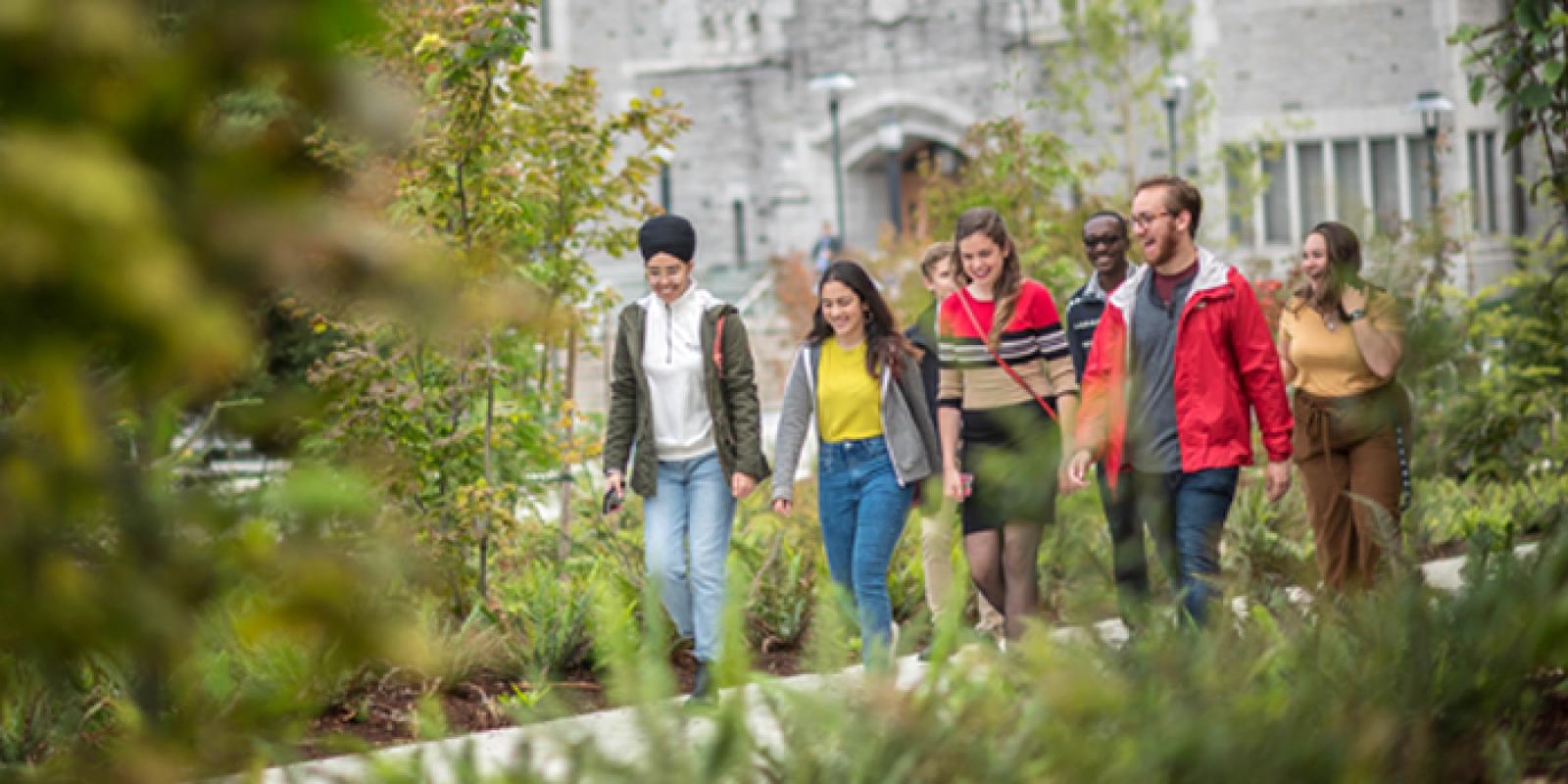 A group of students walking outside, with vegetation in the foreground.