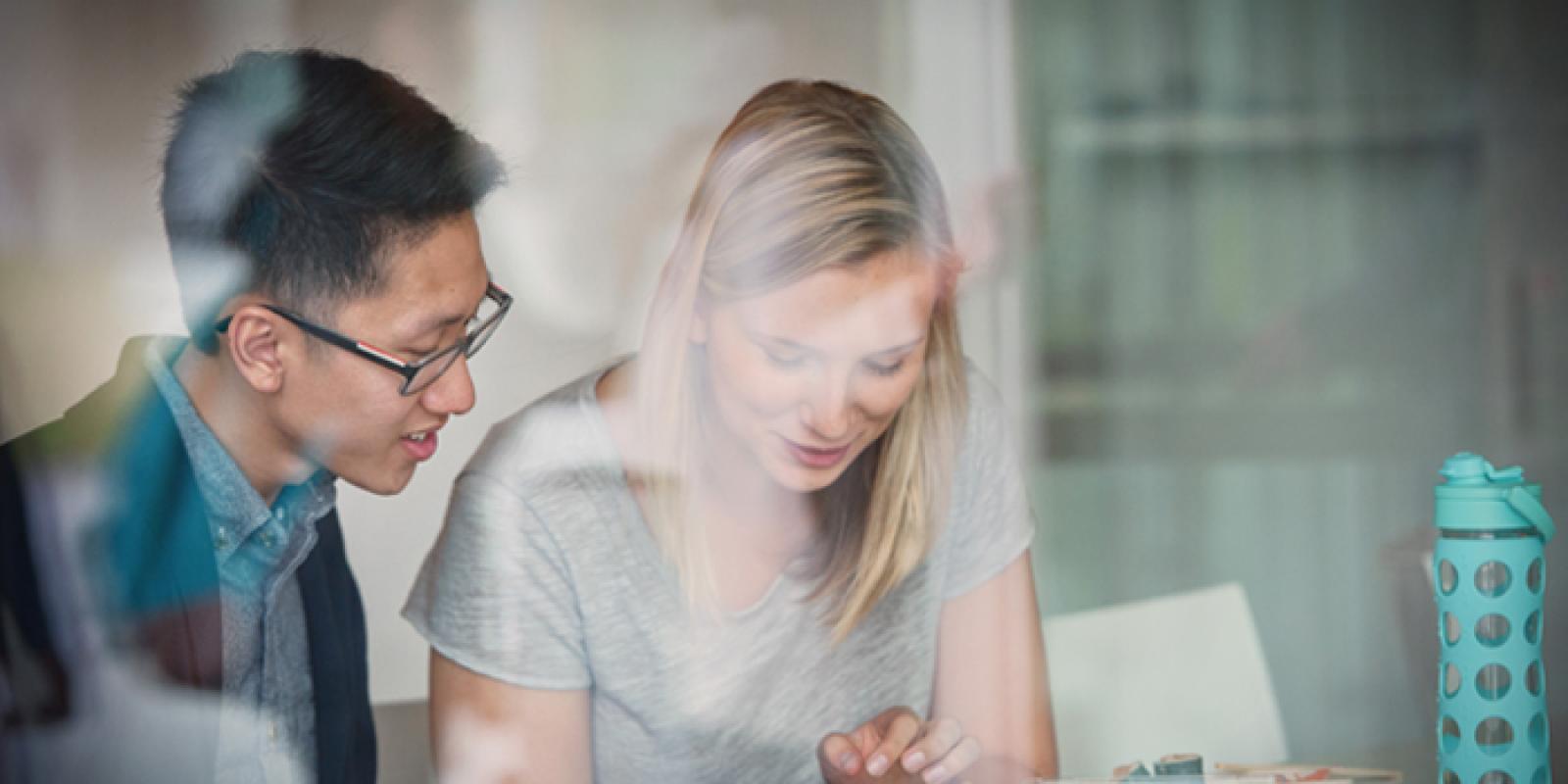 Two people smiling and looking down at presumably a book or laptop.
