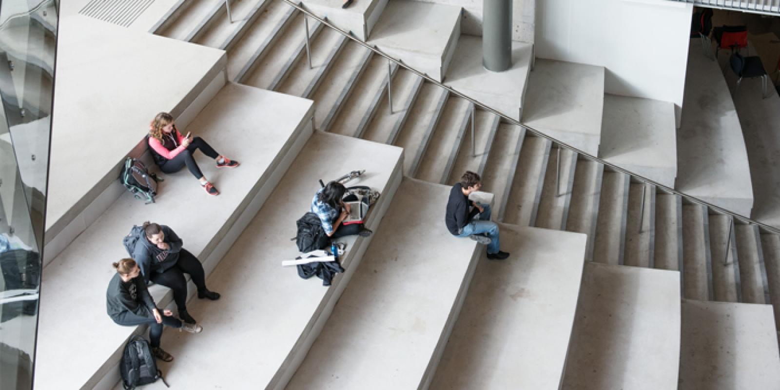 A top-down view of students sitting and studying on large cement steps in the interior of a building.