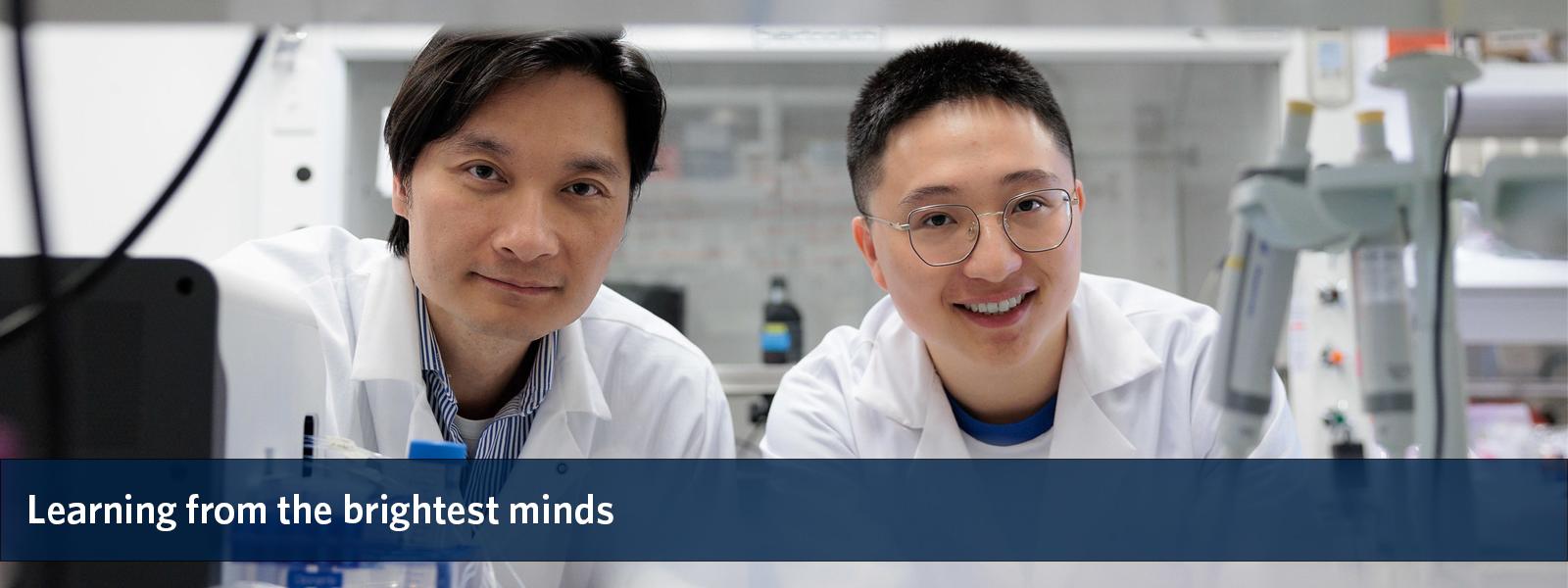 Two researchers in lab coats smiling at the camera, overlaid with the text "Learning from the brightest minds".