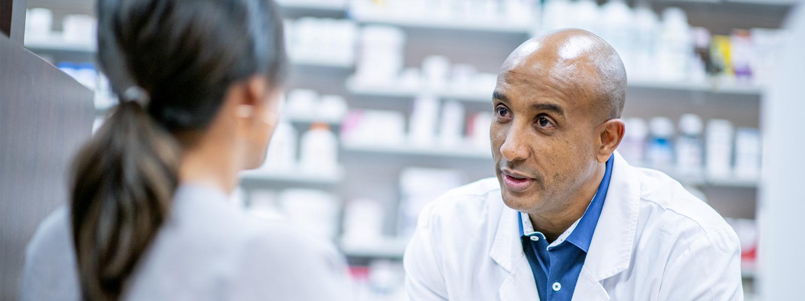 A pharmacist speaking to a patient at the counter of a pharmacy.