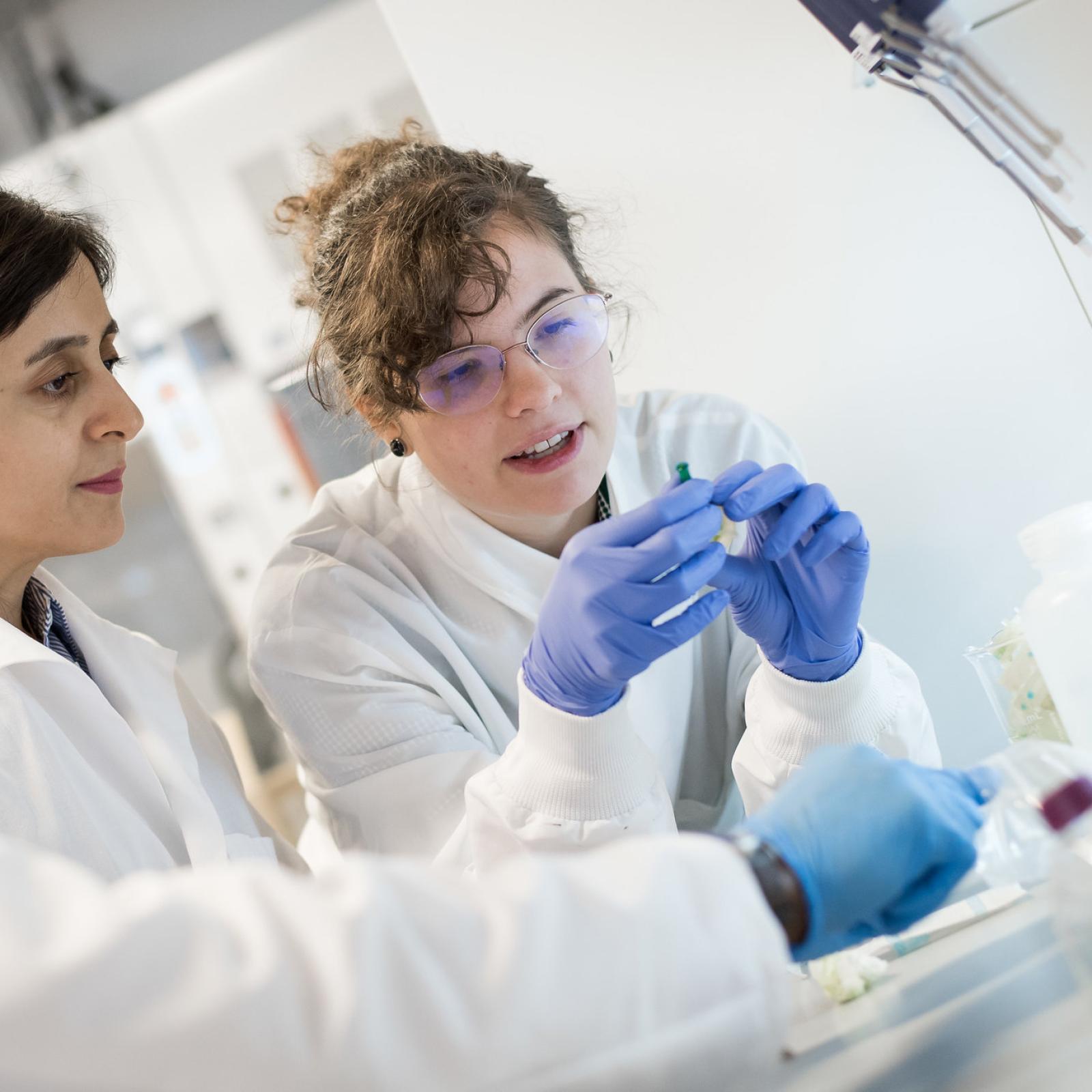 Two students in a lab; they are looking at a piece of equipment that one student is holding.