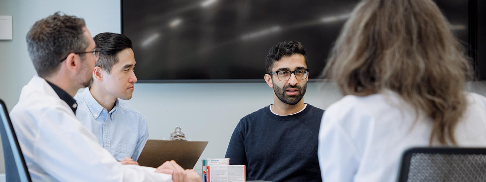 Four health care professionals sitting and conversing, two of whom are wearing lab coats.